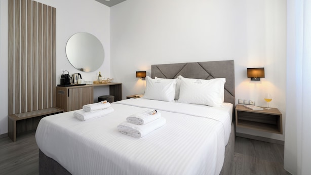 Une chambre d’hôtel moderne avec un grand lit, un banc en bois, un miroir rond et deux tables de chevet avec des lampes.