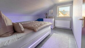 Un dormitorio con cama, cómoda, ventana y radiador.