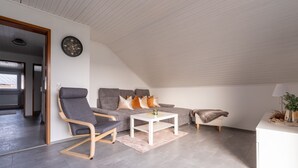 Un dormitorio tipo loft moderno con techo inclinado, un sofá gris, una mesa de centro blanca y un pequeño escritorio blanco.