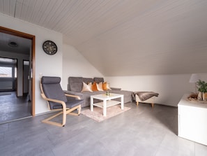 A modern loft bedroom with a sloped ceiling, a gray sofa, a white coffee table, and a small white desk.
