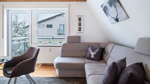 A modern living room with a sectional sofa, a chair, a fireplace, and a view of a building outside. - Apartment 'Schwarzwaldblick D App 10 with Pool, Sauna, Mountain View, Wi-Fi (Schönwald im Schwarzwald)