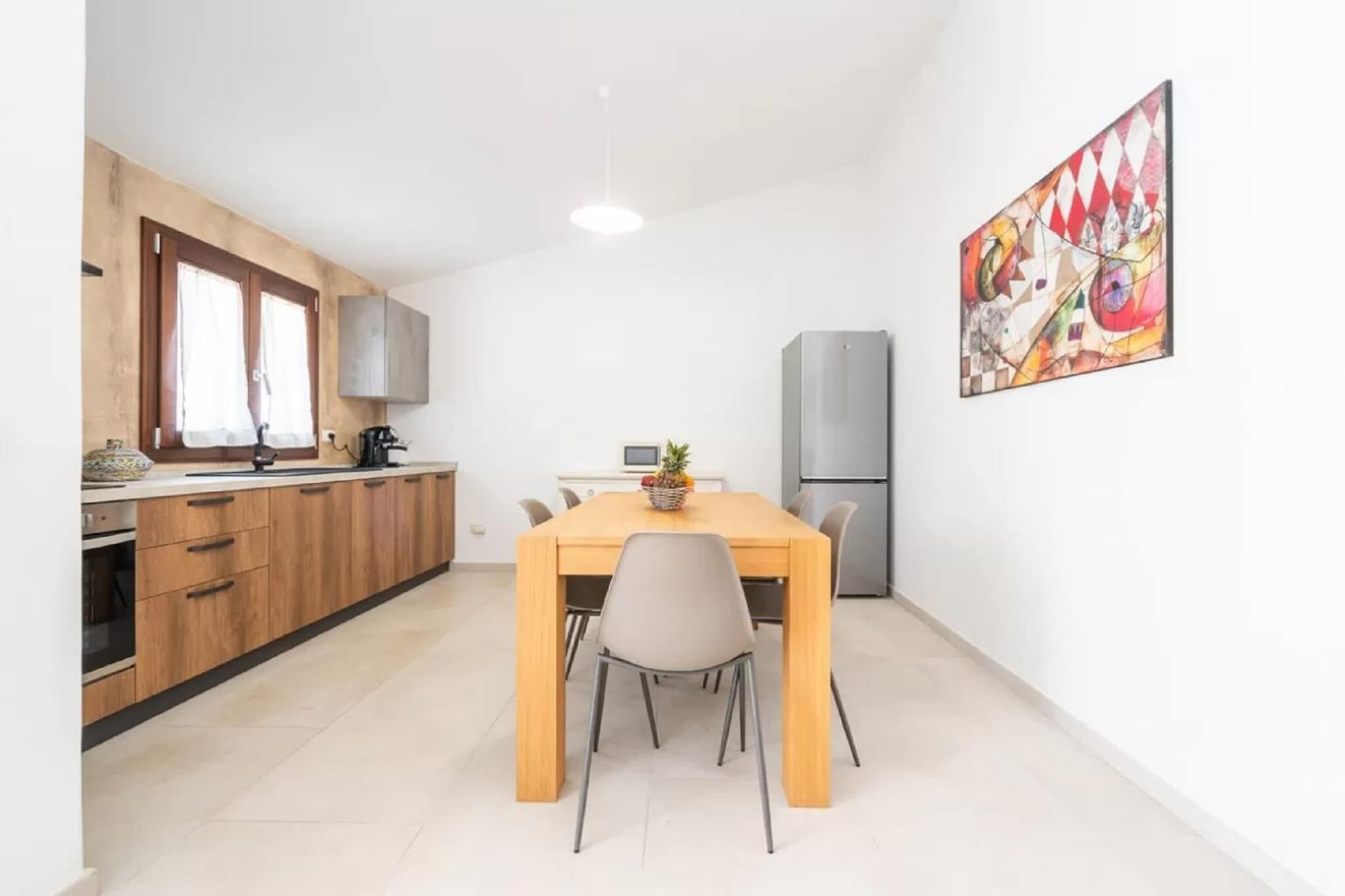 Une cuisine compacte avec des meubles en bois, une table à manger avec des chaises, un réfrigérateur et une œuvre d’art accrochée au mur.