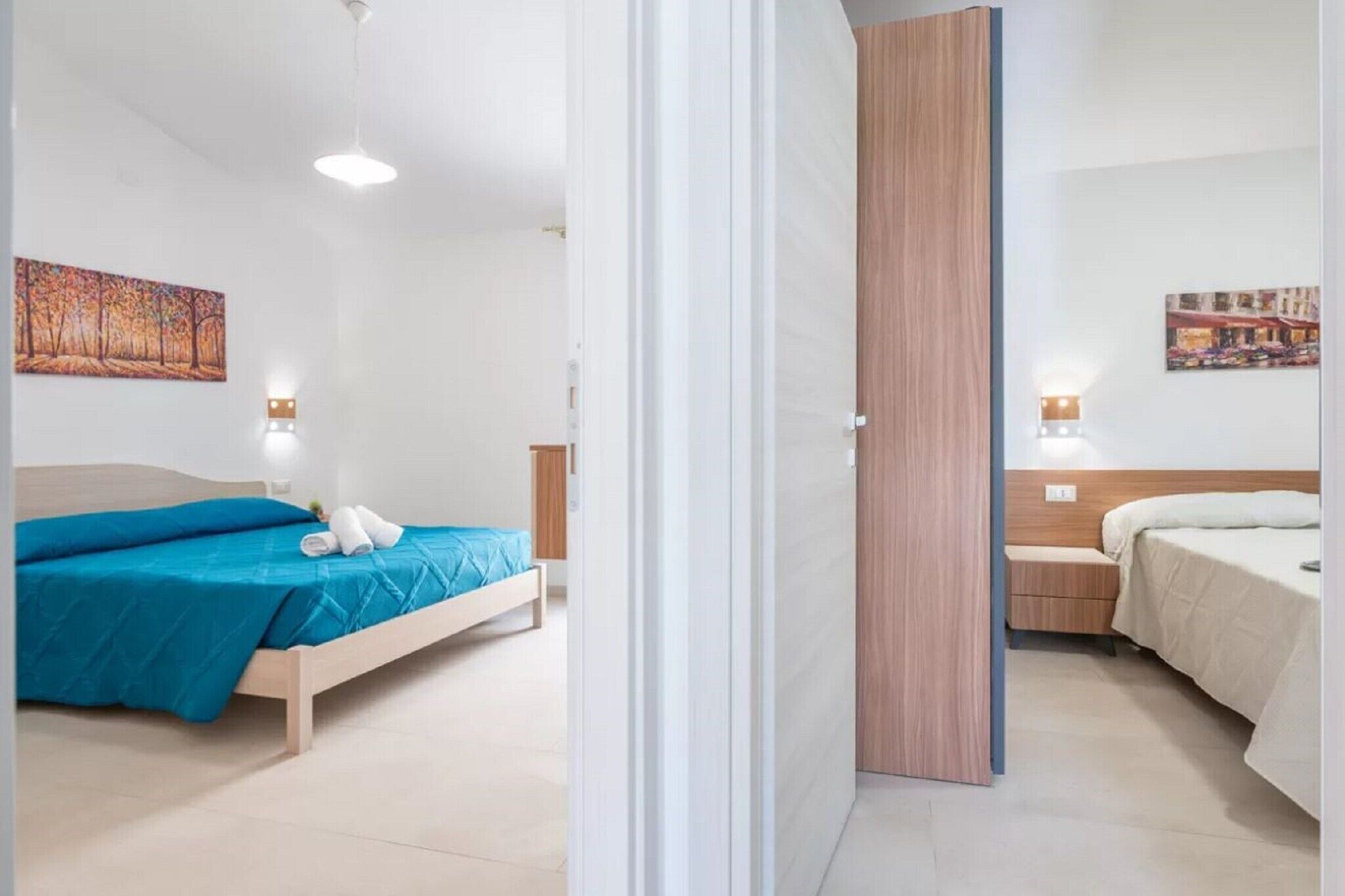 Habitació d'hotel amb dos llits, cada un amb un llençol de color diferent, un armari de fusta i llums penjades a la paret.