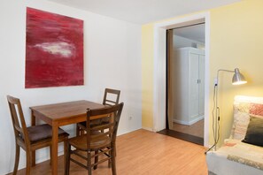 A dining area with a wooden table and chairs, a red abstract painting on the wall, and a doorway leading to another room.