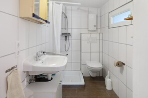A bathroom with a sink, toilet, shower, and a window.