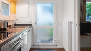 Een compacte keuken met een kookplaat, spoelbak en een dubbele deur met geëtste glazen panelen.