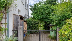 Een poort naar een perceel met een verharde oprit, een houten omheining en weelderige begroeiing.