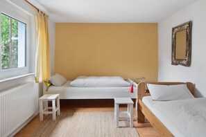 A room with a bed, a window with curtains, a small table, and a mirror on the wall.