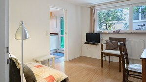 Een kamer met een bed, een bureau, een stoel, een televisie en een raam met uitzicht op bomen.