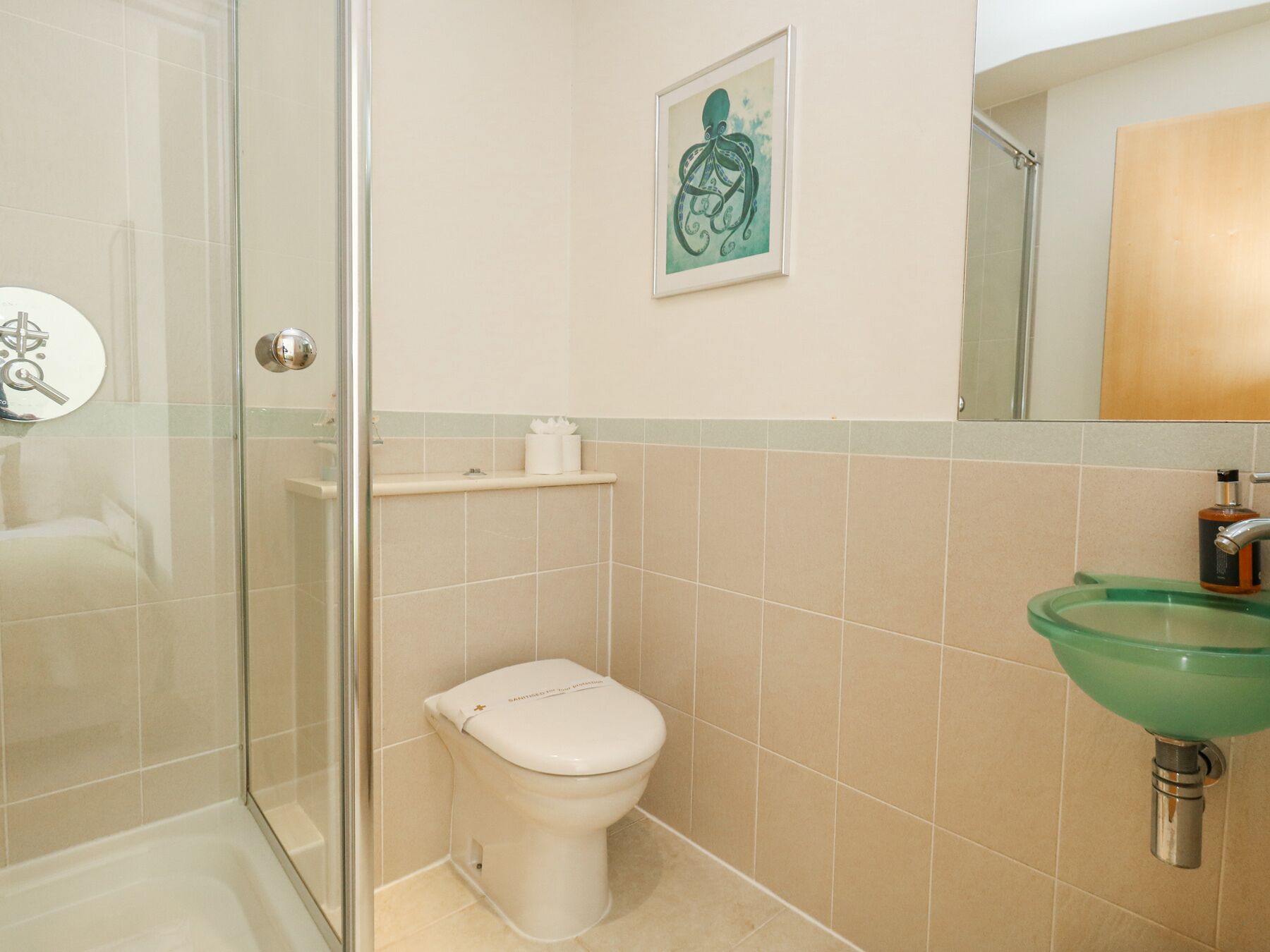 Ein Badezimmer mit Toilette, einer Duschkabine aus Glas, einem grünen Waschbecken und einem gerahmten Kunstwerk an der Wand.