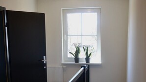 Una escalera con barandilla negra, pared blanca y una ventana con dos plantas en macetas.