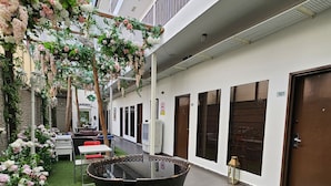 A courtyard with artificial grass, a glass-top table, wicker chairs, and hanging floral arrangements. - V Garden Hotel by Minsu (Kuala Lumpur)