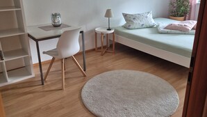 Une chambre à coucher avec un lit, un bureau, une chaise, une lampe, une plante et un tapis rond.