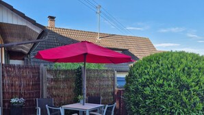 Une terrasse avec une table et des chaises, un parasol rouge et une haie.
