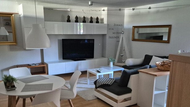 Un salon moderne avec un téléviseur à écran plat, des meubles blancs, une table basse et un canapé.