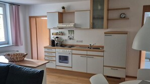 Une cuisine compacte équipée d’une cuisinière, d’un four et d’un évier, un coin repas avec une table et des chaises, et un canapé agrémenté d’un coussin à motifs.