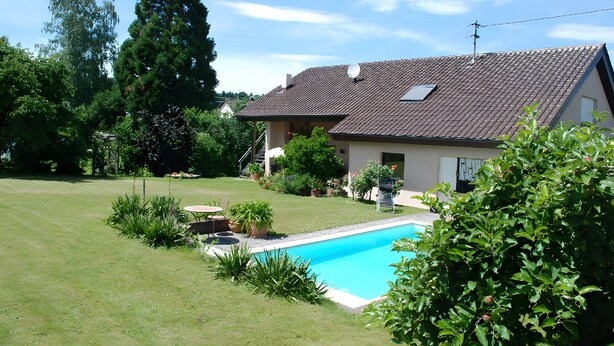 Ein Haus mit Schwimmbad, umgeben von einem gepflegten Rasen und verschiedenen Pflanzen.