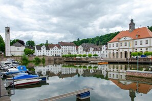 A calm river with boats docked, a church with a tall tower, and traditional buildings with red roofs. - Apartment 'Wohnung 2' with Shared Terrace, Shared Garden and Wi-Fi (Bad Karlshafen)