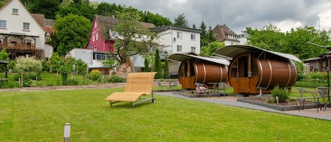 Eine grüne Fläche mit einer Holzbank, einer kleinen Holzhütte und einem großen zylindrischen Gebäude.