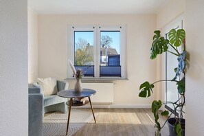 A room with a sofa, a small table, a potted plant, and a window with blinds.