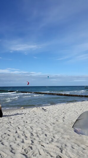 A beach with a sandy shore, a wooden jetty, and a clear sky.