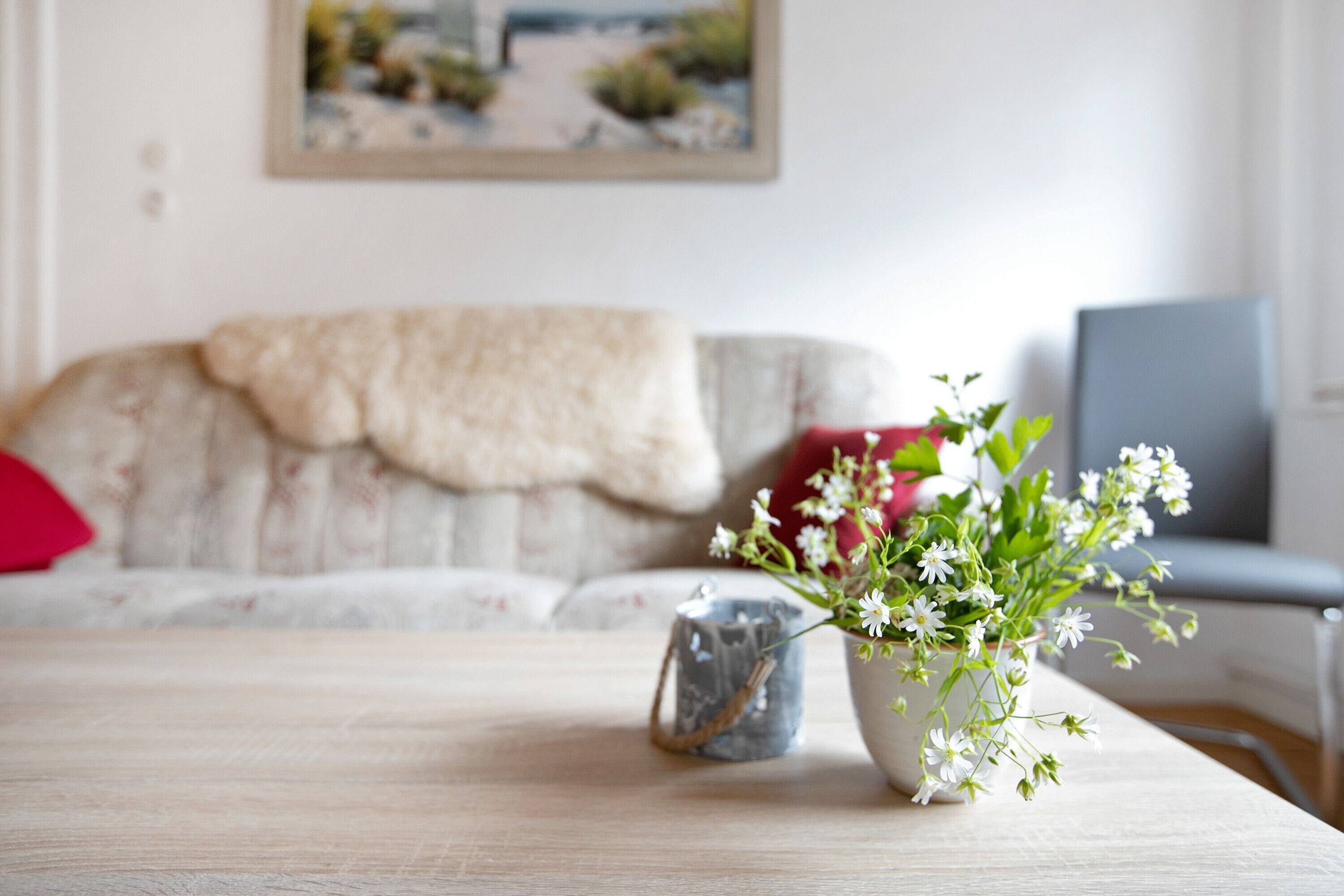 Une table en bois, sur laquelle se trouve un vase rempli de fleurs blanches et un récipient en métal.