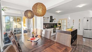 A modern kitchen with a central island, built-in appliances, and a dining area with a wooden table and wicker chairs. - Holiday House with Pool Villa Seabird (Porec)