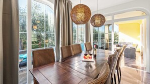 A dining area with a large wooden table, wicker chairs, and two spherical hanging lights. - Holiday House with Pool Villa Seabird (Porec)