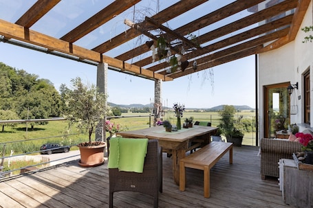 An outdoor deck with a wooden table and chairs, surrounded by potted plants and a view of the countryside.