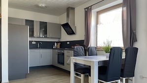 Une cuisine moderne avec des meubles gris, un four encastré et un coin repas comprenant une table et des chaises blanches.