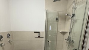 Une salle de bain avec une douche à parois de verre, un lavabo blanc et un petit tabouret.
