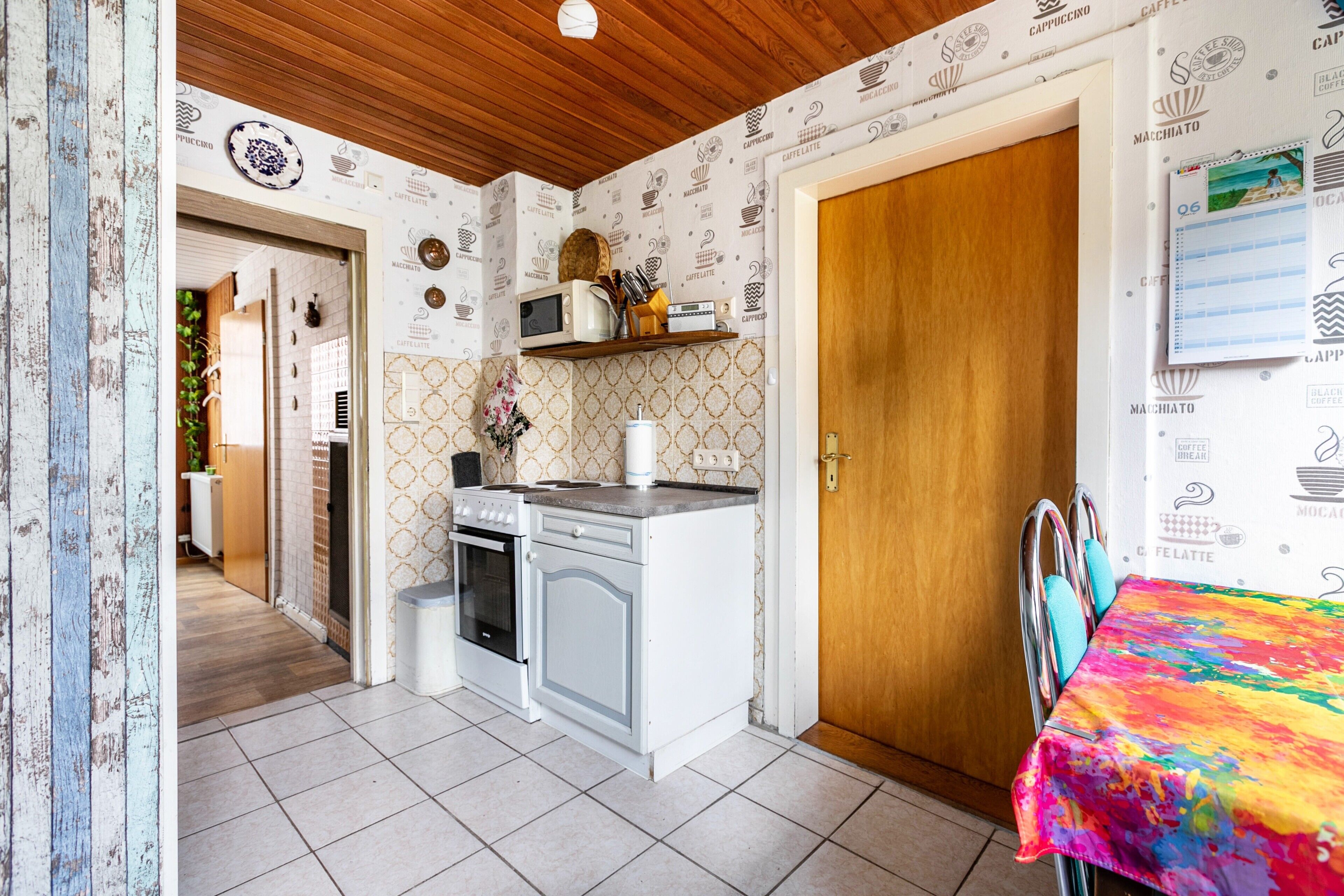 Una cocina con microondas, estufa y lavaplatos, una puerta de madera y un mantel colorido.