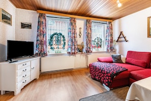 Una habitación con una televisión sobre un tocador blanco, un sofá rojo y una ventana con cortinas.