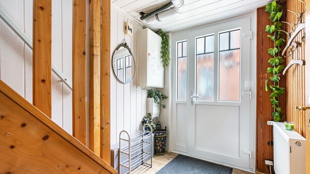 Una escalera de madera que lleva a una puerta blanca, con un espejo, un radiador y una planta.