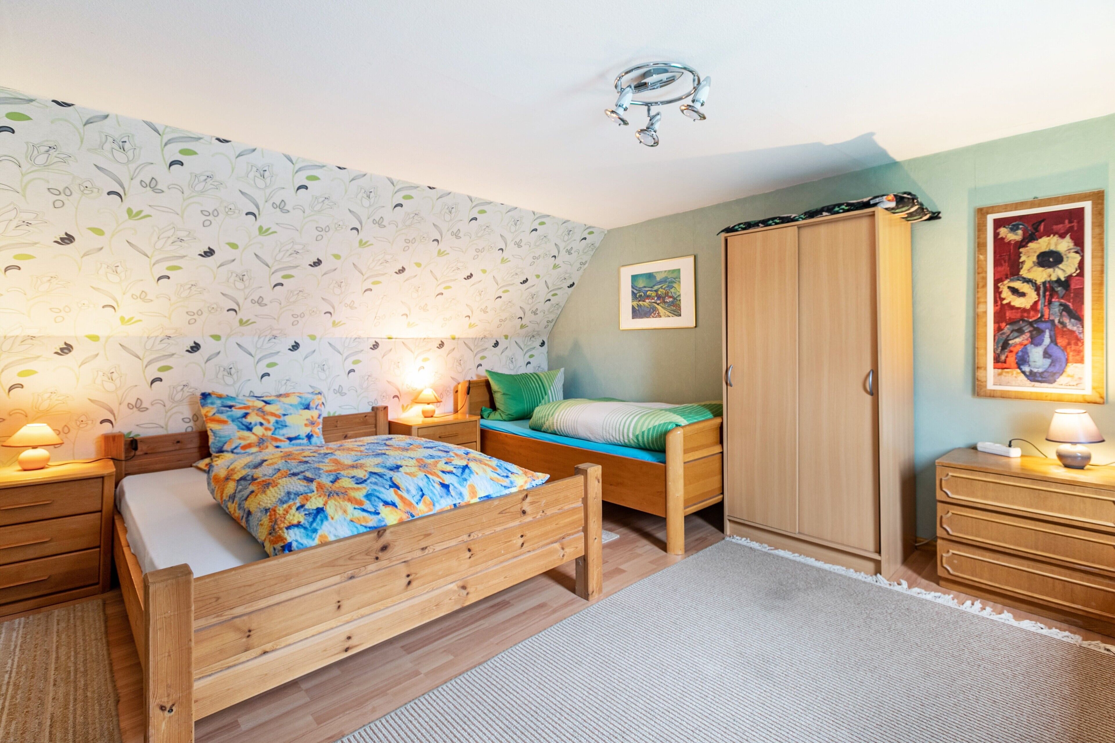 A bedroom with a wooden bed, bedside tables with lamps, a wardrobe, and a floral-patterned wallpaper.