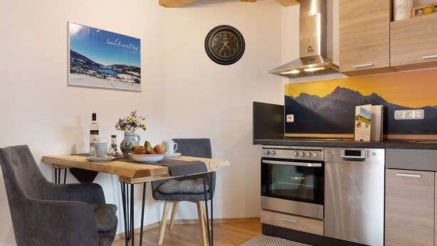 Een moderne keuken met een eethoek, houten kastjes, een fornuis en een klok aan de muur.