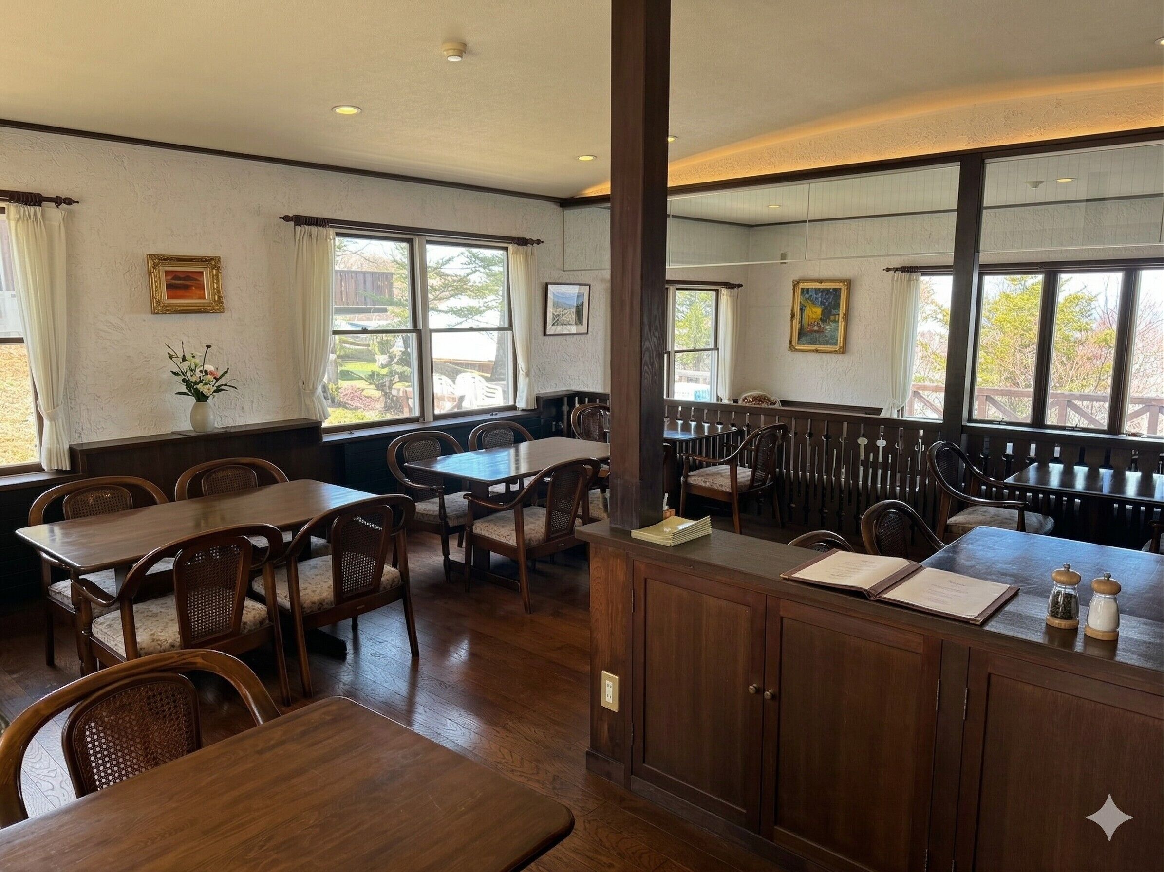 A restaurant with wooden tables and chairs, large windows, and a view of the outdoors.