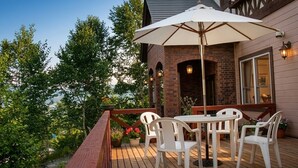 Une terrasse en bois avec une table et des chaises, un grand parasol et, au fond, un bâtiment en briques.