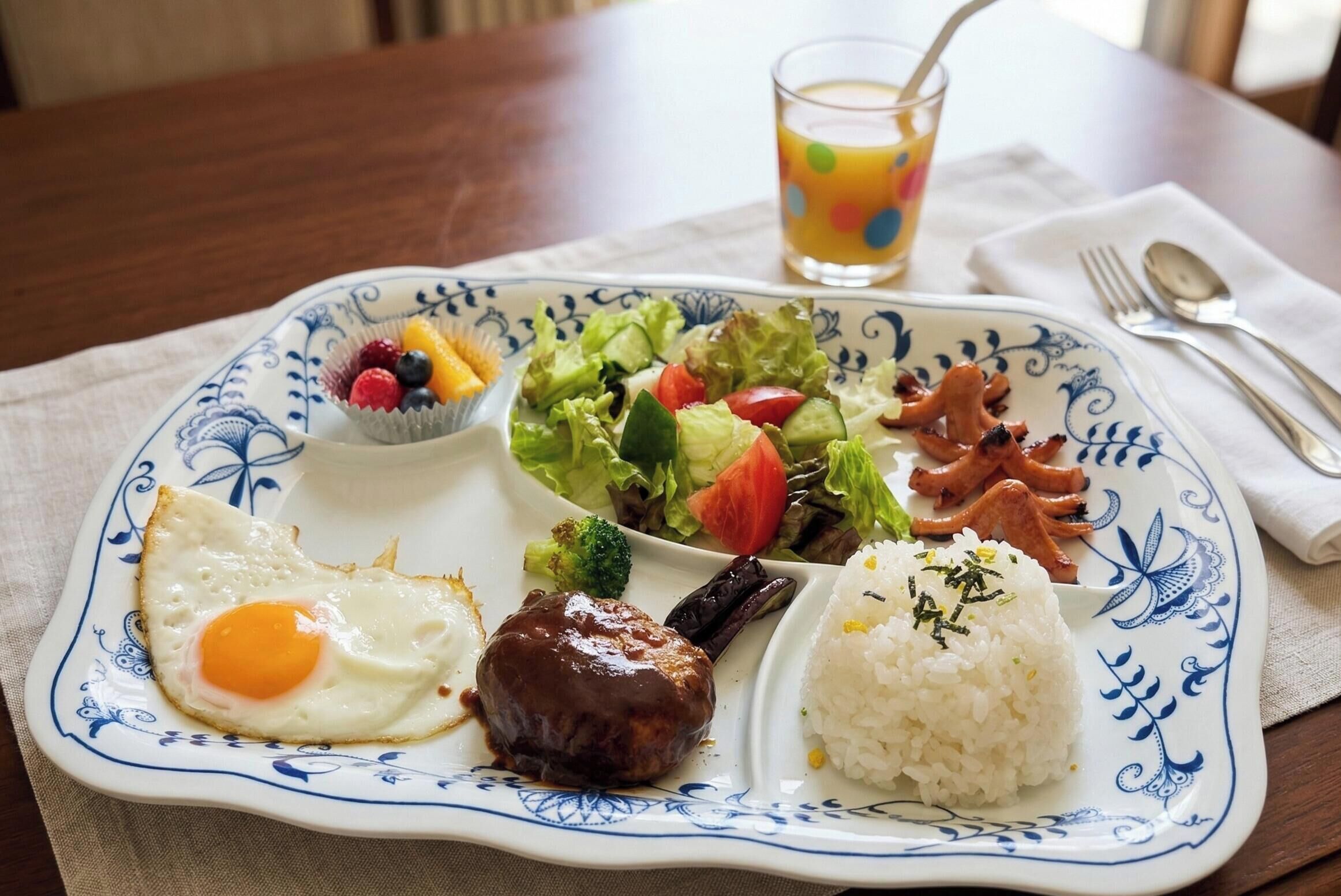 Un plato con un huevo frito, carne, arroz, ensalada y un vaso de jugo.