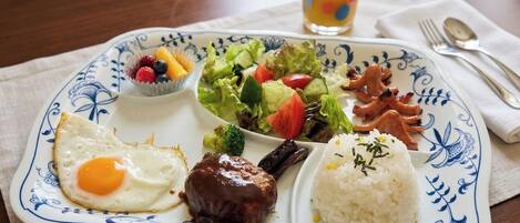 A plate with a fried egg, meat, rice, salad, and a cup of juice.