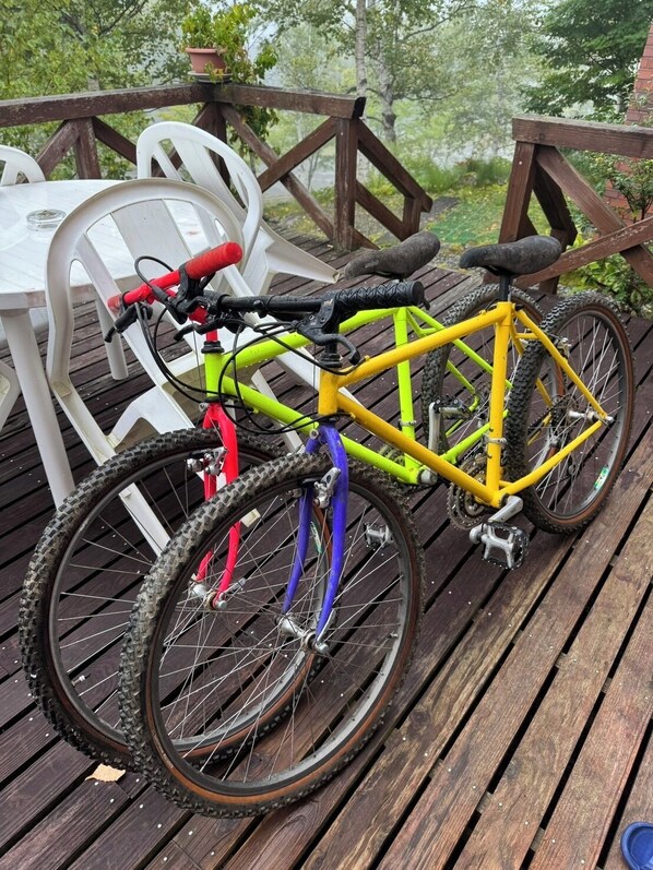 A bicycle parked on a wooden deck with a railing, surrounded by white plastic chairs.