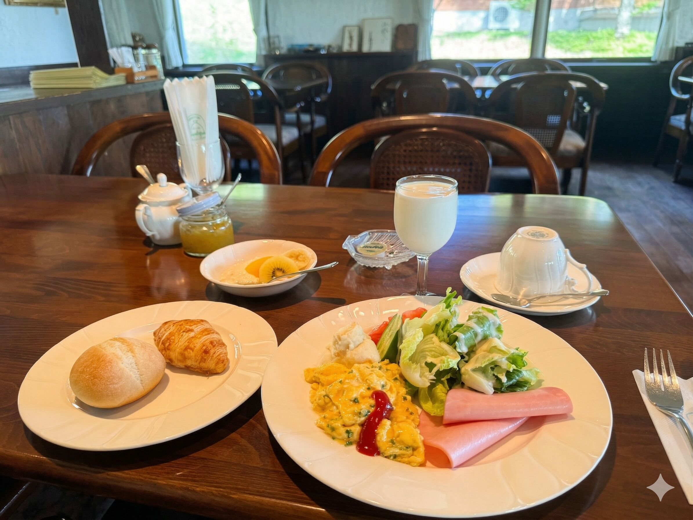 A dining table with breakfast items including eggs, ham, and a salad, a teapot, and a milk glass.