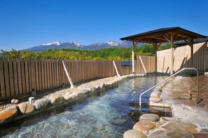 A hot spring area with a wooden fence, stone steps, and a wooden pavilion.