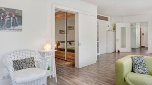 A modern living room with a white sofa, a green sofa, a white wicker chair, and a wooden floor.