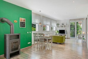 A modern living room with a green wall, a fireplace, a dining area with white chairs, and a TV. - Apartment 'Paffendorf' with Shared Terrace and Wi-Fi (Gutach (Schwarzwaldbahn))