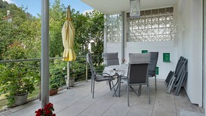 A covered patio with a table and chairs, potted plants, and a view of greenery.