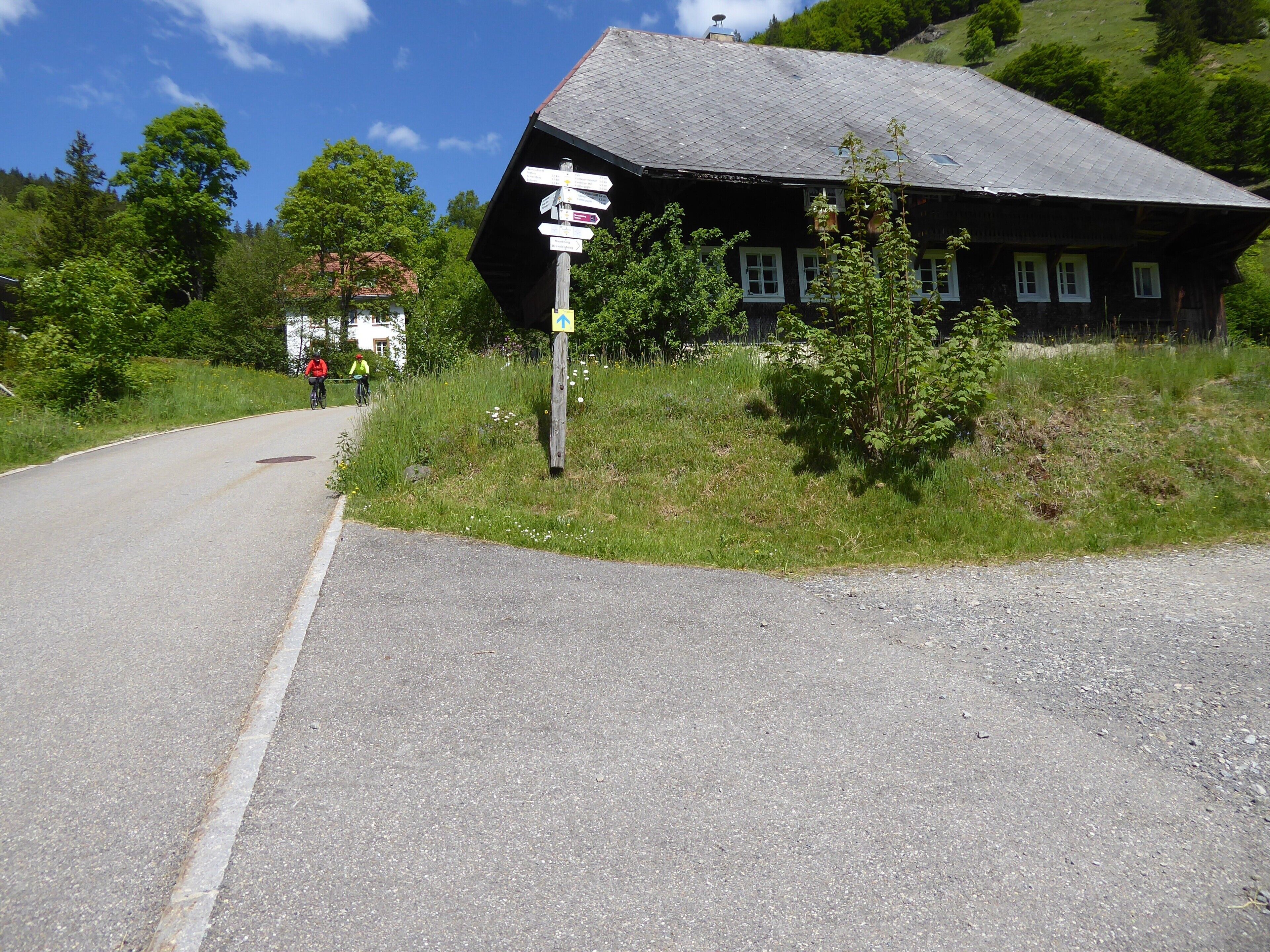 Eine ländliche Straße mit Wegweiser und einem traditionellen Haus mit Schindeldach.