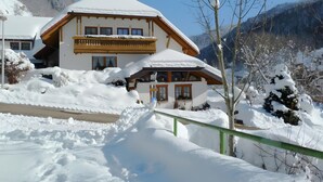 Un edificio de estilo chalet con techo nevado, balcones de madera y un paisaje de montañas al fondo.
