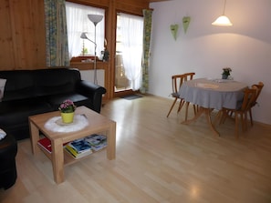 Une pièce comprenant un canapé noir, une petite table en bois avec une plante, une table à manger avec des chaises et une lampe.