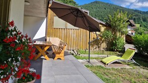 Une terrasse avec une table et des chaises, un parasol et une vue sur une montagne boisée.